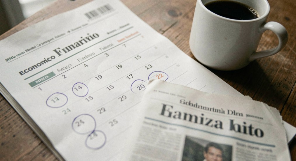 Calendario economico cartaceo con date cerchiate, giornale finanziario italiano sfocato e tazza di caffè
